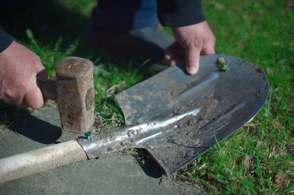 Male hands with hammer fixing a broken shovel, outdoors close-up